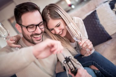 Oturma odasında kanepede oturan genç romantik çift şarap içip aşık keyfini çıkarın.