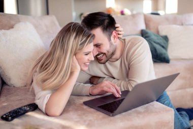 Genç çift kanepede dizüstü bilgisayarla dinleniyor. Aşk, mutluluk, insanlar ve eğlence konsepti..