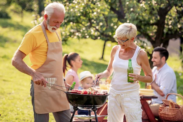 Barbecue time. The older couple is standing by the grill and having fun while making lunch.