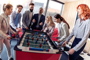 İş adamları birlikte harika vakit geçiriyorlar. Meslektaşlar modern ofiste masa futbolu oynuyorlar..