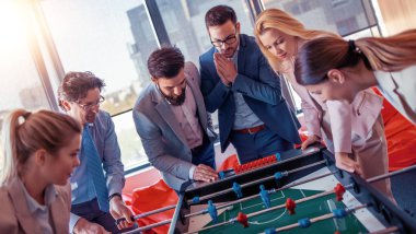 İş adamları birlikte harika vakit geçiriyorlar. Meslektaşlar modern ofiste masa futbolu oynuyorlar..
