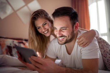 Genç bir çift, bir otel odasında yatarken tablet kullanıyor..