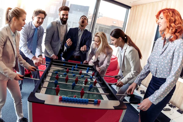 Business people having great time together.Colleagues playing table football in modern office.