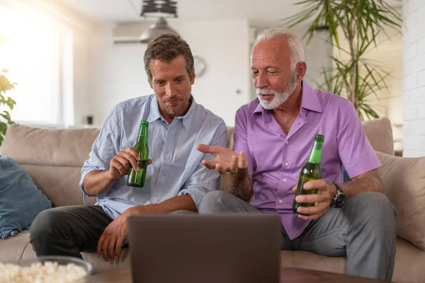 Father and son drink beers and watching football game at home.