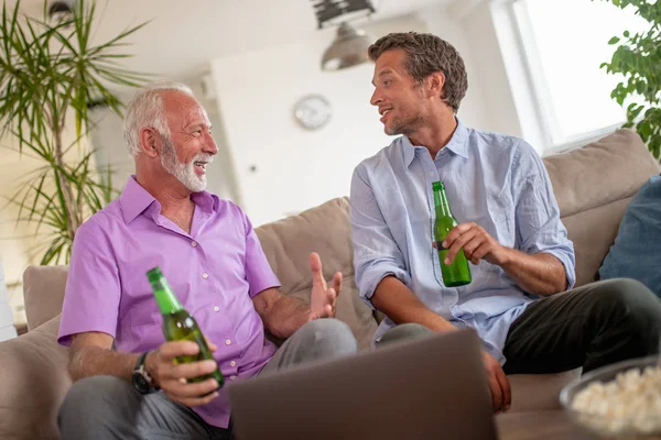 Father and son drink beers and watching football game at home.