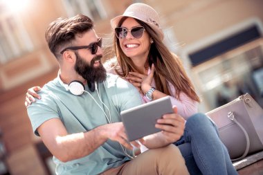 Bankta oturan ve tablet ve kulaklık ile müzik dinlemek sevgi dolu genç Çift.