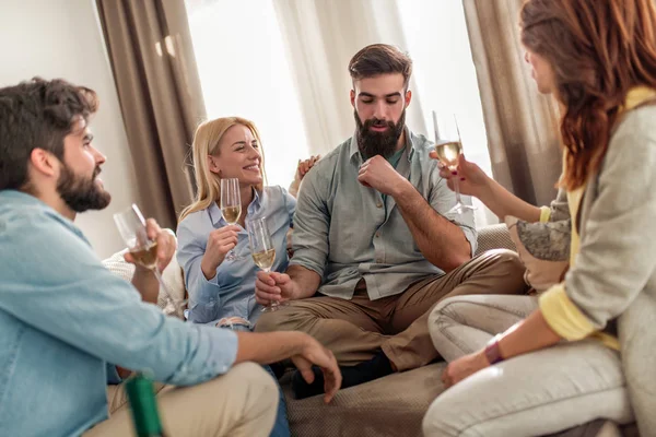 Cheerful  group of  friends sitting on a sofa at home, enjoying conversation and drinking whine.