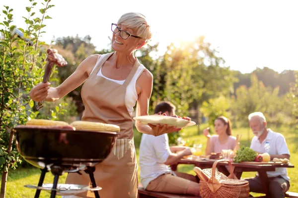 人和家庭时间观念 夏季花园聚会上烧烤烤架上的资深女性烹饪肉 — 图库照片