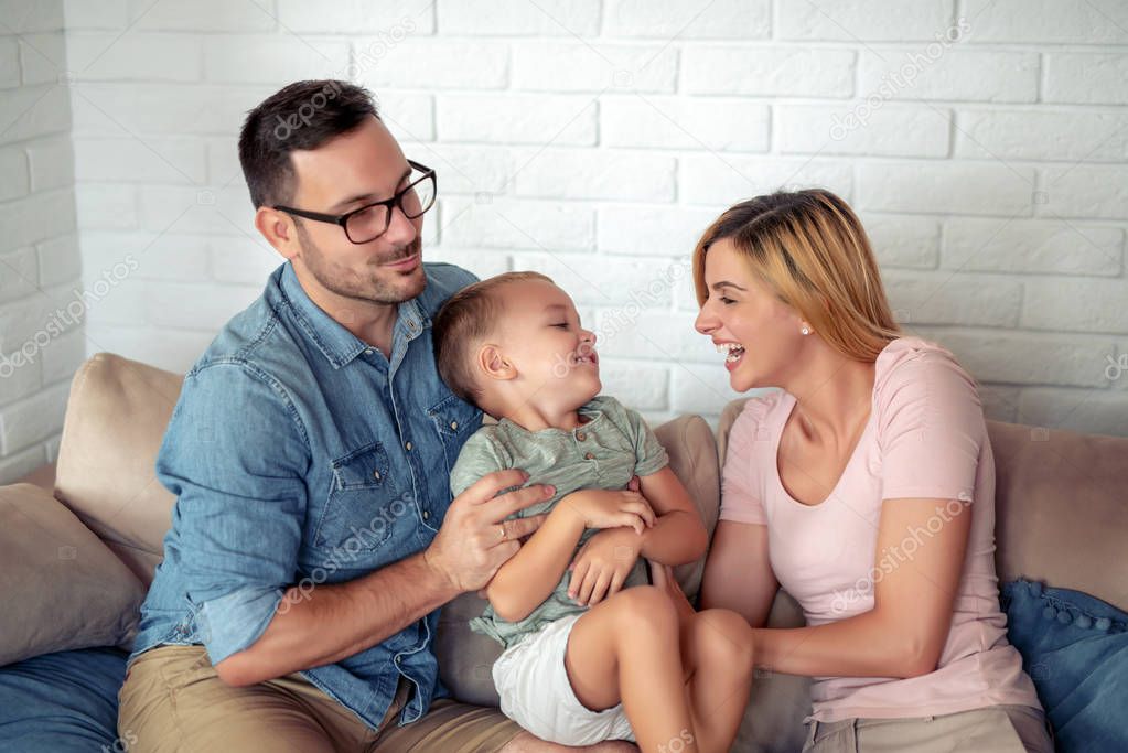 Happy family sitting on sofa laughing together. Cheerful parents playing with their son at home. 