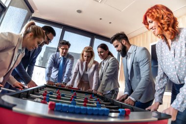 İş adamları birlikte harika vakit geçiriyorlar. Meslektaşlar modern ofiste masa futbolu oynuyorlar..