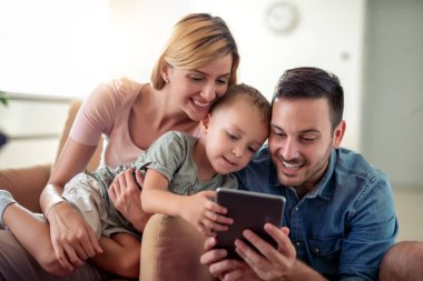 Mutlu aile birlikte evde zevk, tablet kullanma ve birlikte iyi vakit geçiriyor.