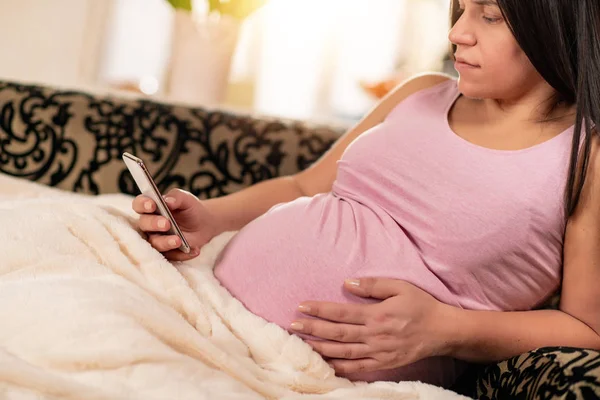 Έγκυος Γυναίκα Κάθεται Στον Καναπέ Και Χρήση Του Τηλεφώνου — Φωτογραφία Αρχείου