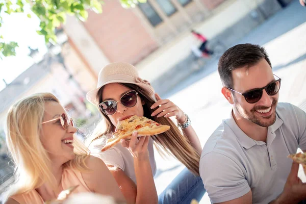 Happy group of people eating pizza outdoors,they are enjoying together.