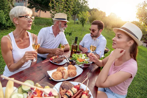 Happy family having lunch and drink wine in the garden on a sunny day.