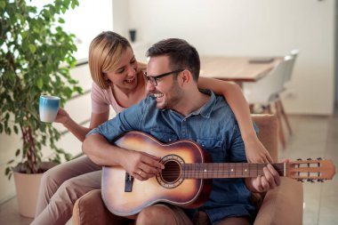 Yakışıklı adam kendi evinde kız arkadaşı gitar oynuyor.