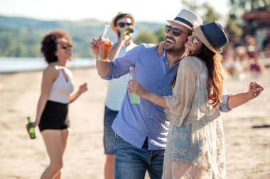 Gülümseyen arkadaş grubu plajda bira şişeleri clinking.