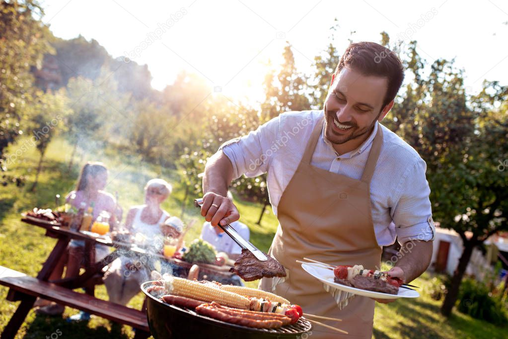 Food, people and family time concept.Young man cooking meat on barbecue grill at summer party.