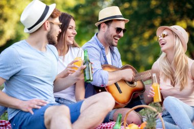 Mutlu arkadaş grubu parkta eğleniyor ve gülümsüyor. Gitar çalıp şarkı söylerler..