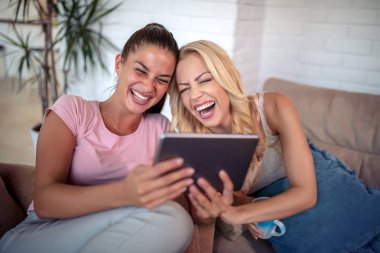 Evde tablet kullanan mutlu genç bayan arkadaşlar..