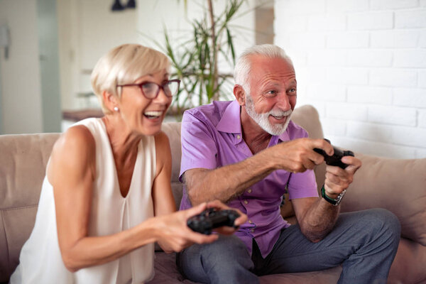 Happy senior couple sitting together in their living room and playing video games.