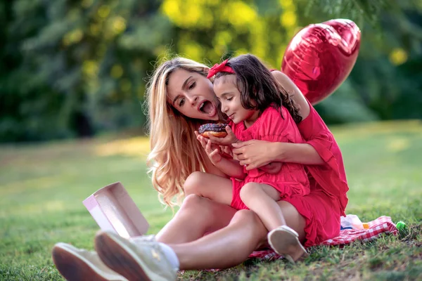 母と彼女の娘は ドーナツを食べて 夏の公園で楽しんでいます — ストック写真