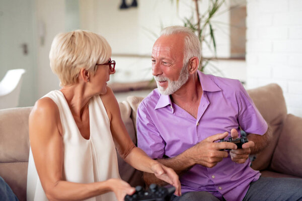 Happy senior couple sitting together in their living room and playing video games.