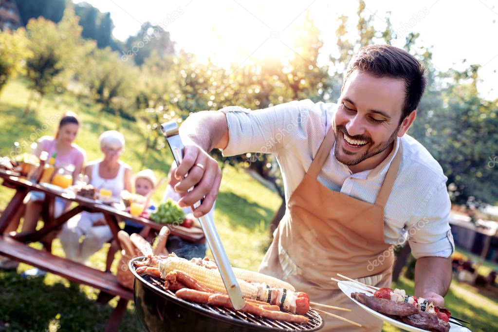 Food, people and family time concept.Young man cooking meat on barbecue grill at summer garden  party.
