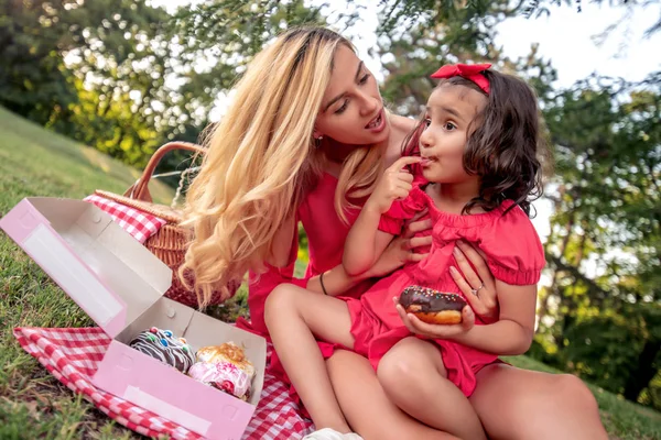 母と彼女の小さな娘は楽しんで 公園でドーナツを食べて — ストック写真