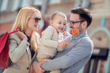 Şehirde yürüyen alışveriş çantaları ve lolipop ile mutlu bir aile. Satış, tüketicilik ve aile kavramı.