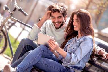 Genç çift, park bankında oturan ve tablet ile eğleniyor. Aşk, insanlar, eğlenceli ve mutluluk kavramı.