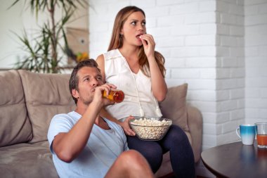 TV izlerken, patlamış mısır ve içki elma şarabı bir koltukta evde yemek Çift.