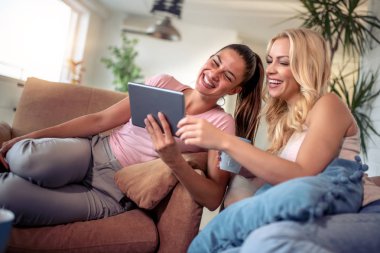 Evde tablet kullanan mutlu genç bayan arkadaşlar..