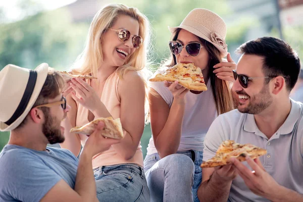 Happy friends eating pizza, having fun outdoors. Dating, consumerism, food, lifestyle concept.