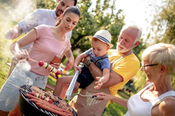 Happy big family gathered around the grill at picnic. Leisure,food,family and holidays concept.