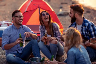 Bir grup genç arkadaş sahilde eğleniyor, kamp yaparken bira içiyor ve gitar çalıyor..