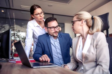 İş adamları ofiste çalışırken dizüstü bilgisayar kullanıyor ve gülümsüyor..