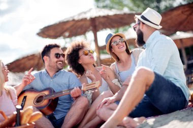 Sahilde parti olan, gitar çalan bir grup arkadaş.