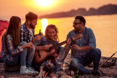 Bir grup genç arkadaş sahilde eğleniyor, kamp yaparken bira içiyor ve gitar çalıyor..
