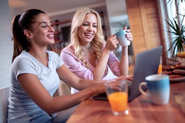 iki genç kadın bir dizüstü bilgisayar ile mutfakta.