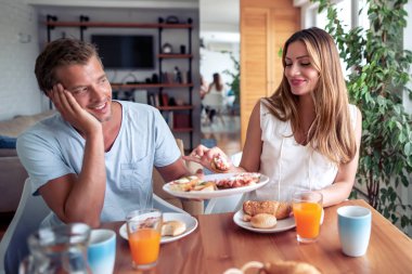 Mutfakta masada otururken kahvaltı eden genç ve sevgi dolu bir çiftin portresi.