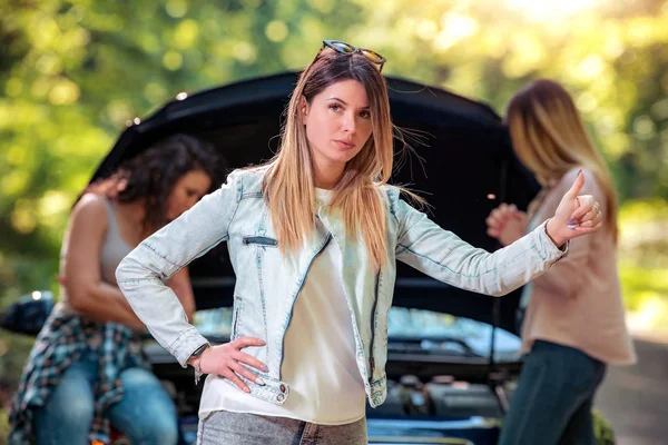 Car breakdown-woman hitchhiking thumbing while her friends  tries to fix car.