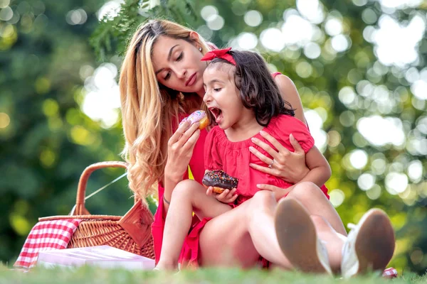 若い母と彼女の娘は 公園でドーナツを食べて 楽しみを持っています — ストック写真