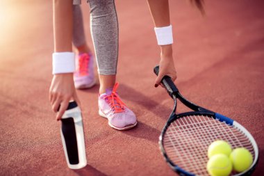 Tenis topu ve raket ile tenis oyuncusu hizmet vermeye hazırlanıyor. Tenis kortundaki kız bir şişe su alıyor.