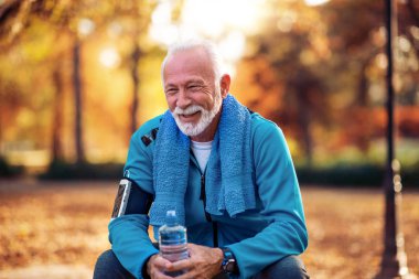 Boynunda havlu ile Kıdemli adam içme suyu ve parkta açık egzersiz sonrası dinlenme