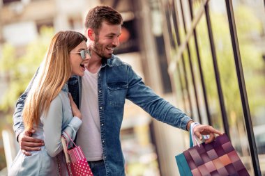Şehirde vitrin yakınında yürüyen alışveriş çantaları ile mutlu genç çift 