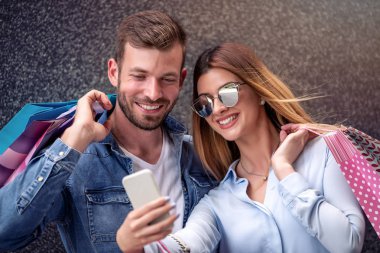 Mutlu çift selfie smartphone ile alarak alışveriş torbaları ile