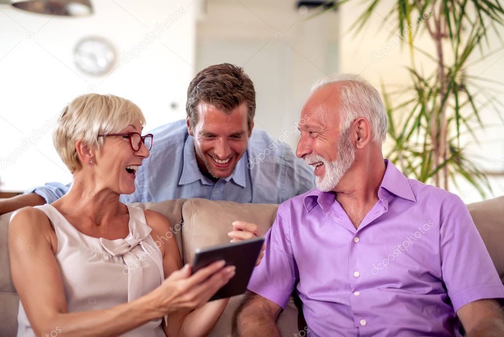 Senior couple with their son using digital tablet at home.