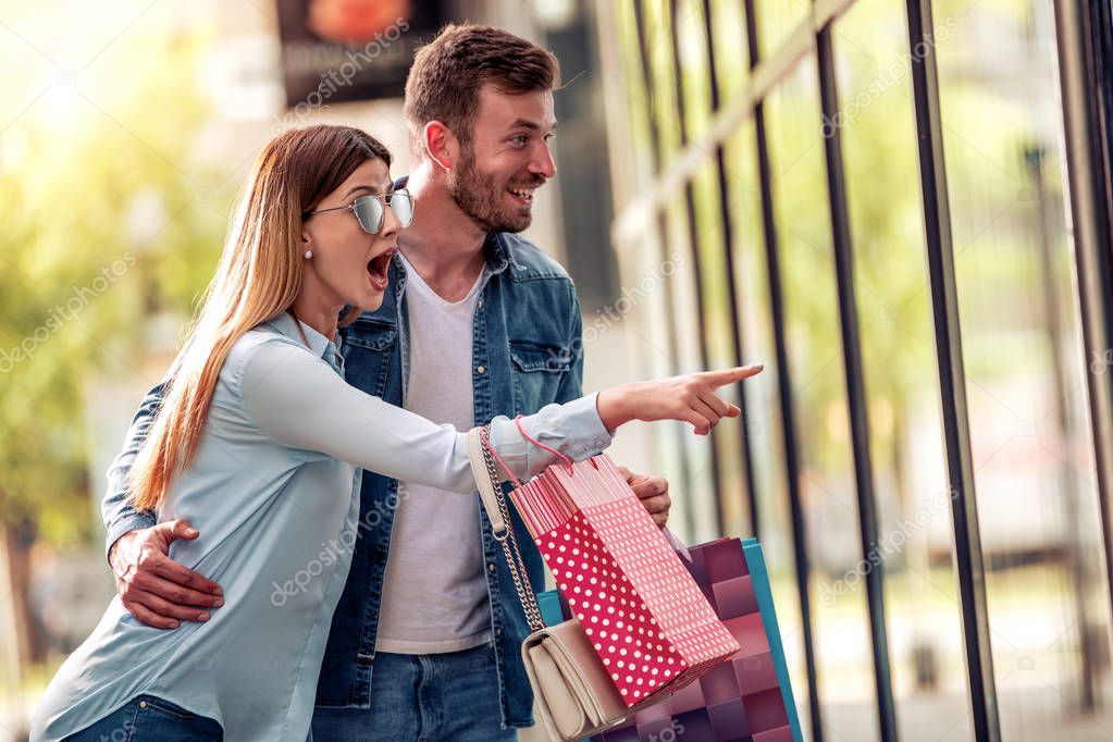 Happy young couple with shopping bags walking near shop window in city 