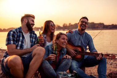 Arkadaşlarla vakit geçirmek. Genç ve mutlu insanlar gitar çalarken birlikte oturuyorlar..