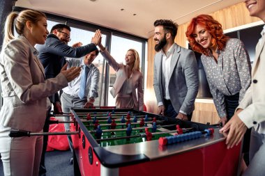 İş adamları birlikte harika vakit geçiriyorlar. Meslektaşlar modern ofiste masa futbolu oynuyorlar..